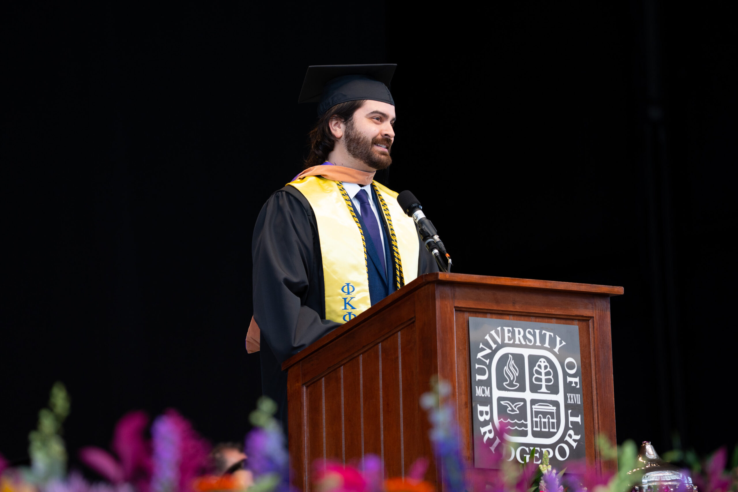Man in graduation gown speaking at a podium.