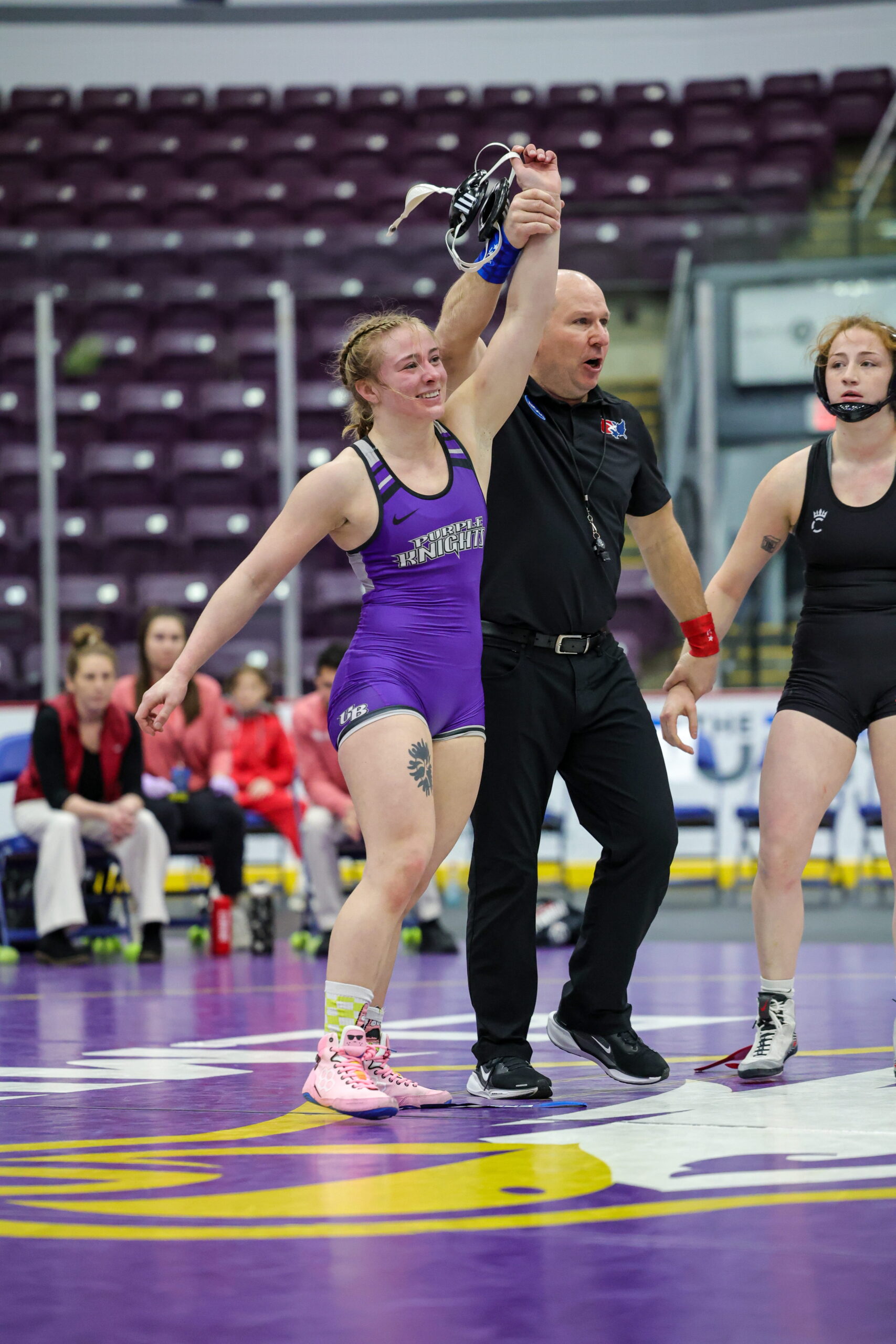 A wrestling match concludes with a referee raising the arm of a victorious wrestler in a purple singlet.