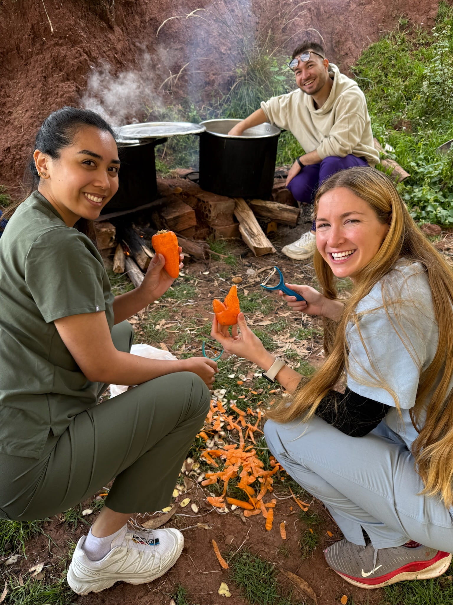 Three PA students kneeling around a large pot over a fire pit.