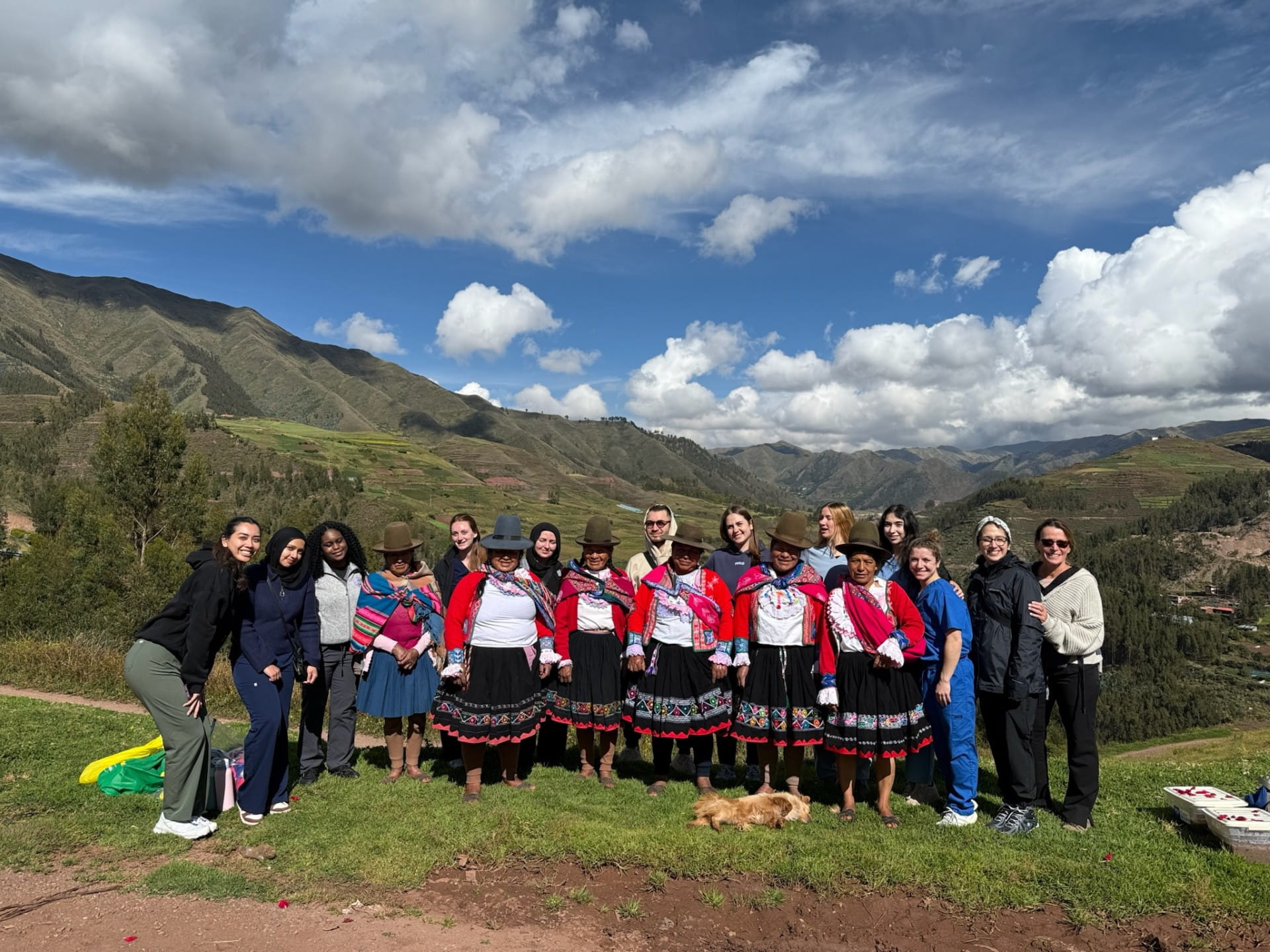 UB PA students posing for a photo with six Peruvian Women with the Peruvian highlands in the background.