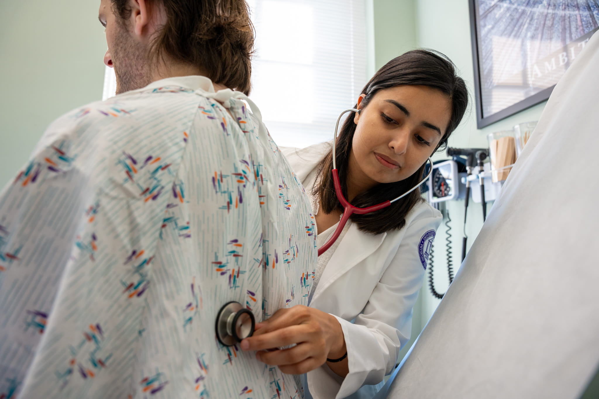A PA student uses a stethoscope while examining a patient.