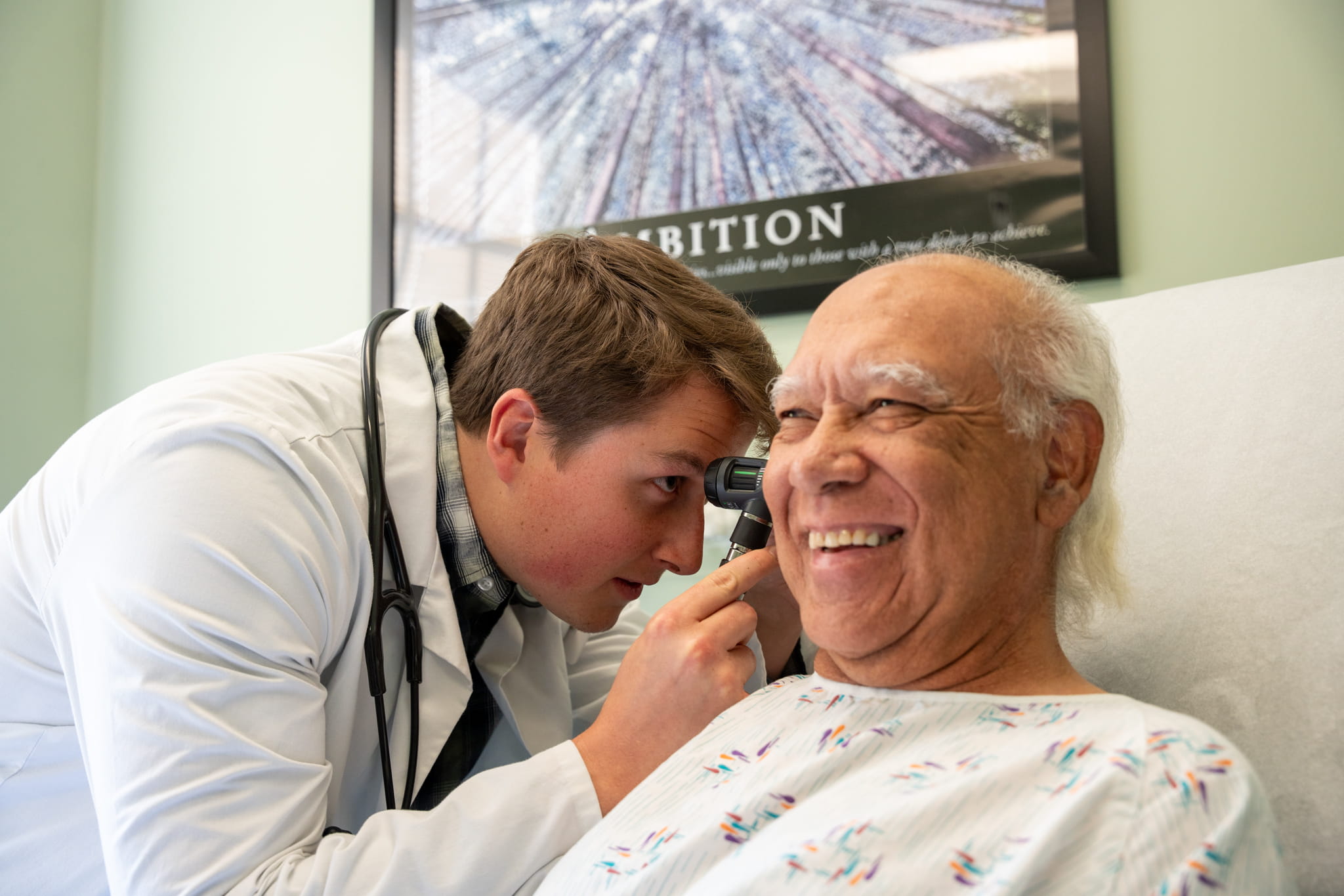A PA student looks inside a patient’s ear using an otoscope.