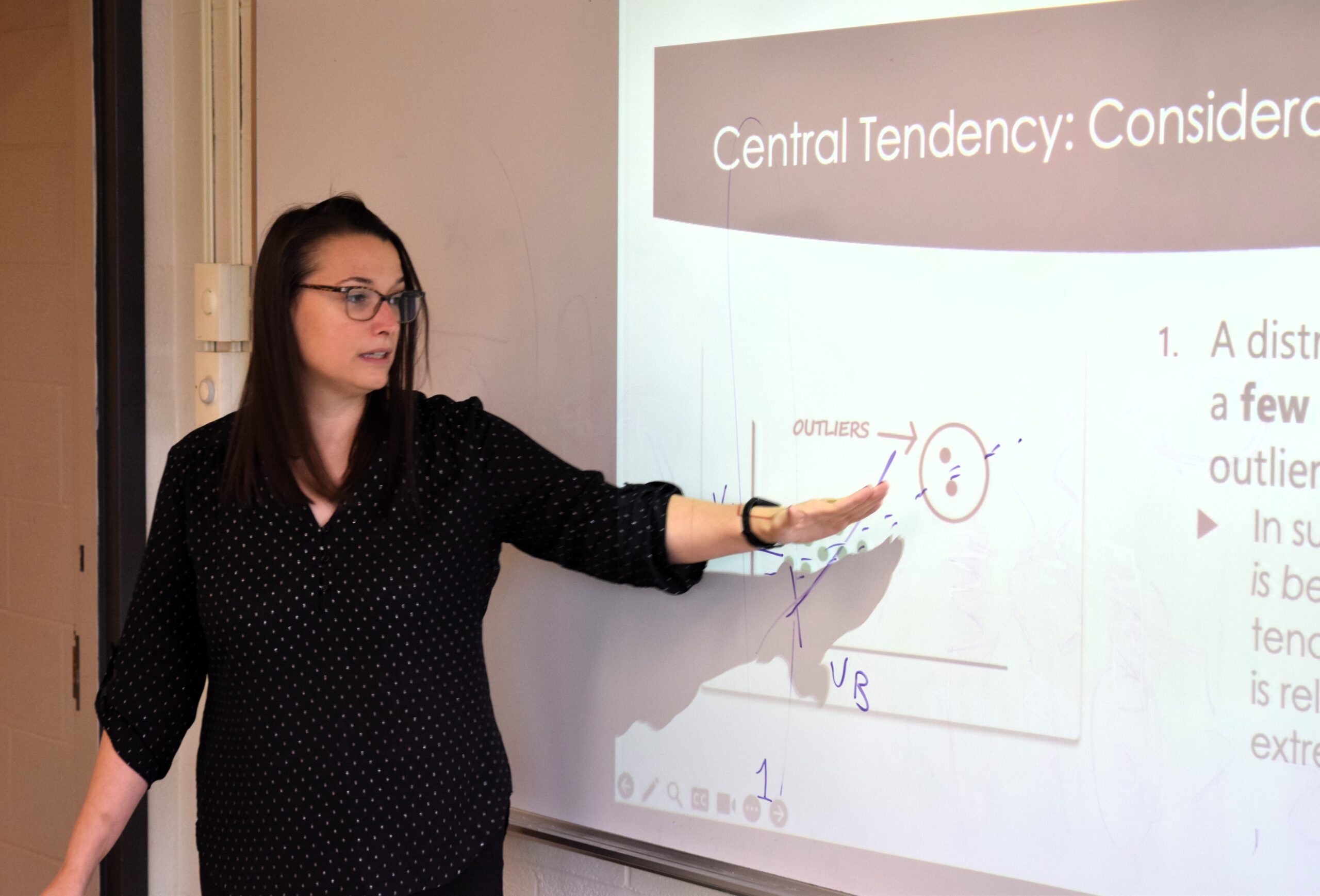 Professor giving a lecture gesture to a graph displayed on a whiteboard