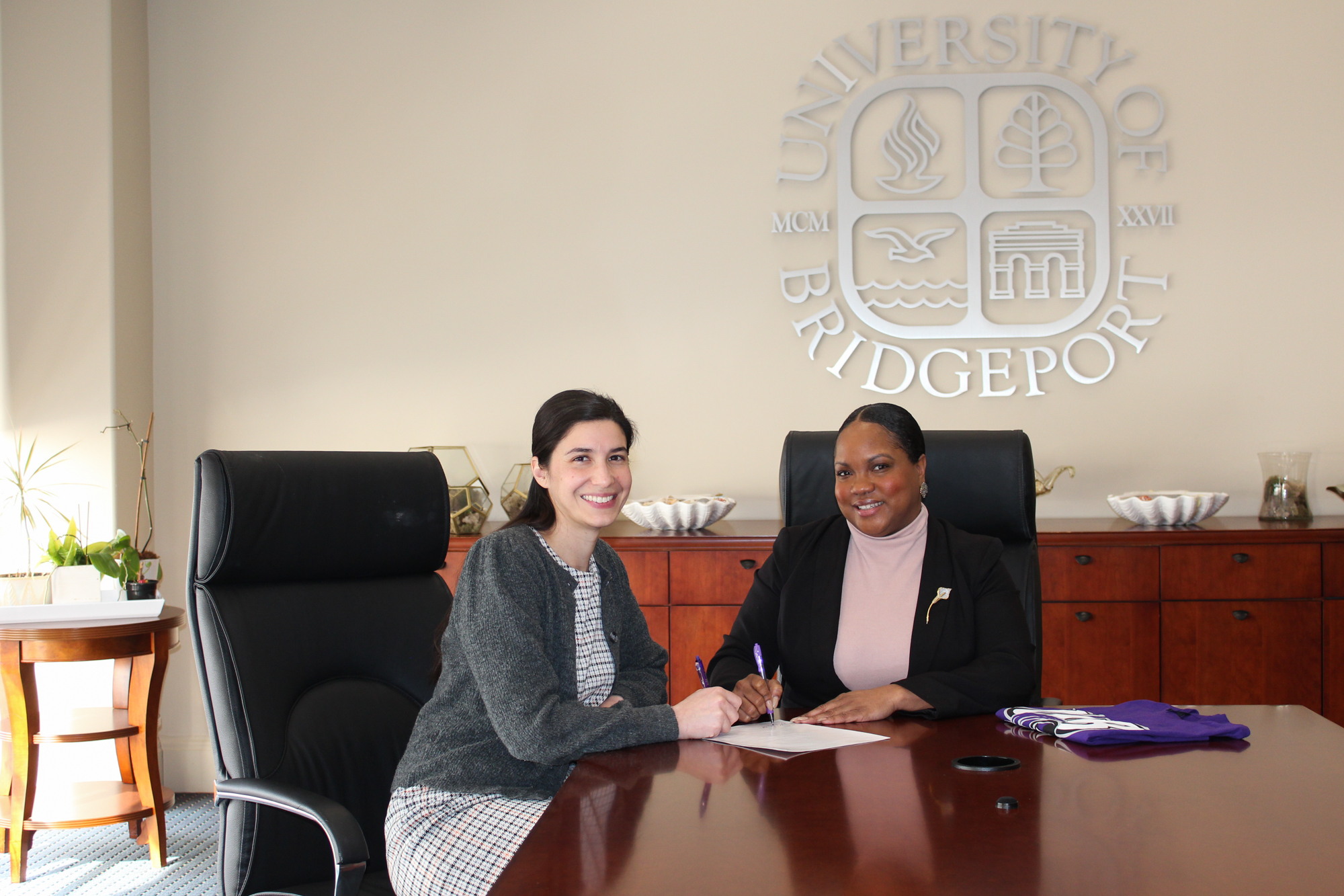 Two women sitting at a conference table signing a piece of paper.