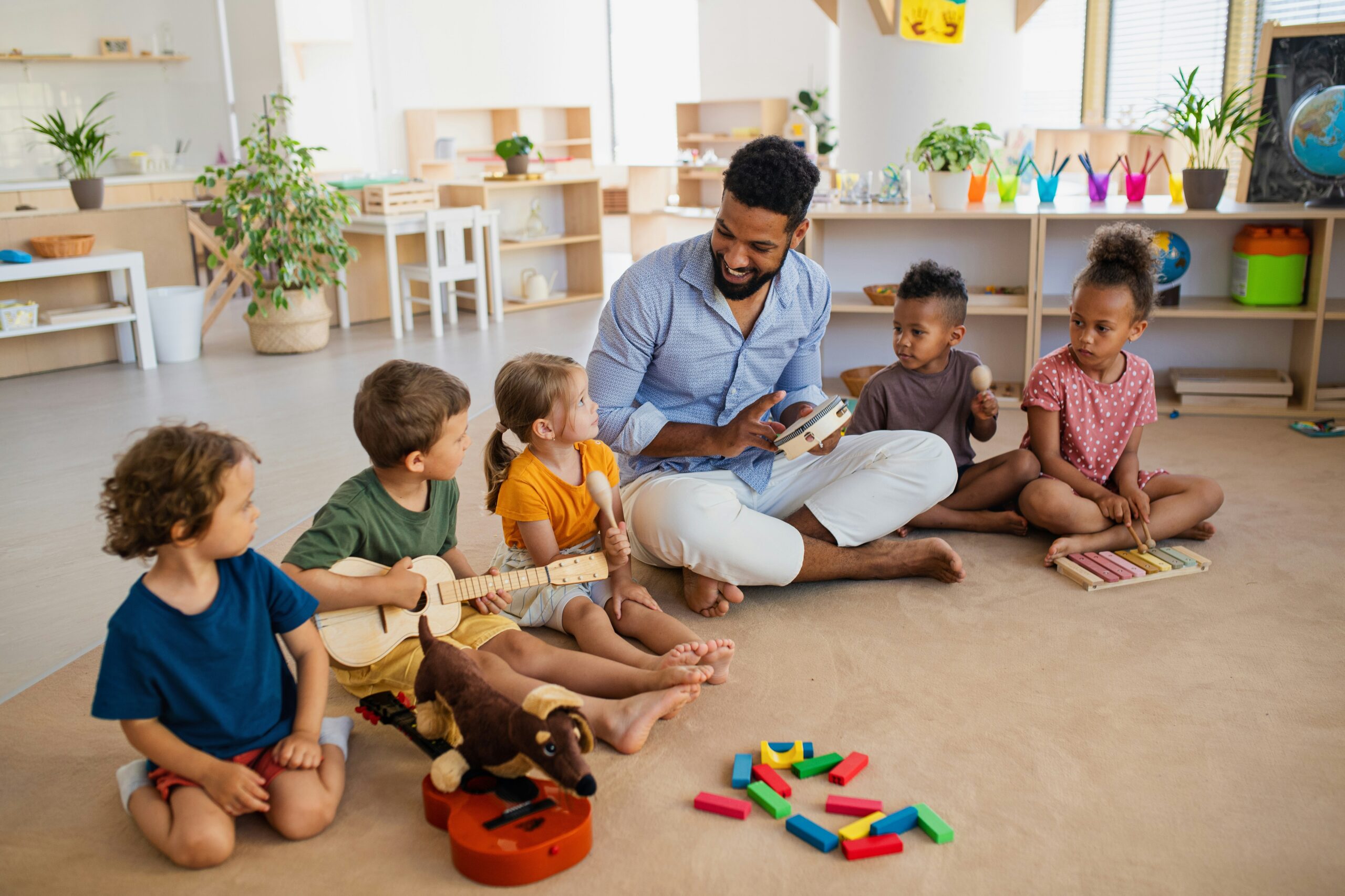 A group of small children sit on the floor with their teacher.