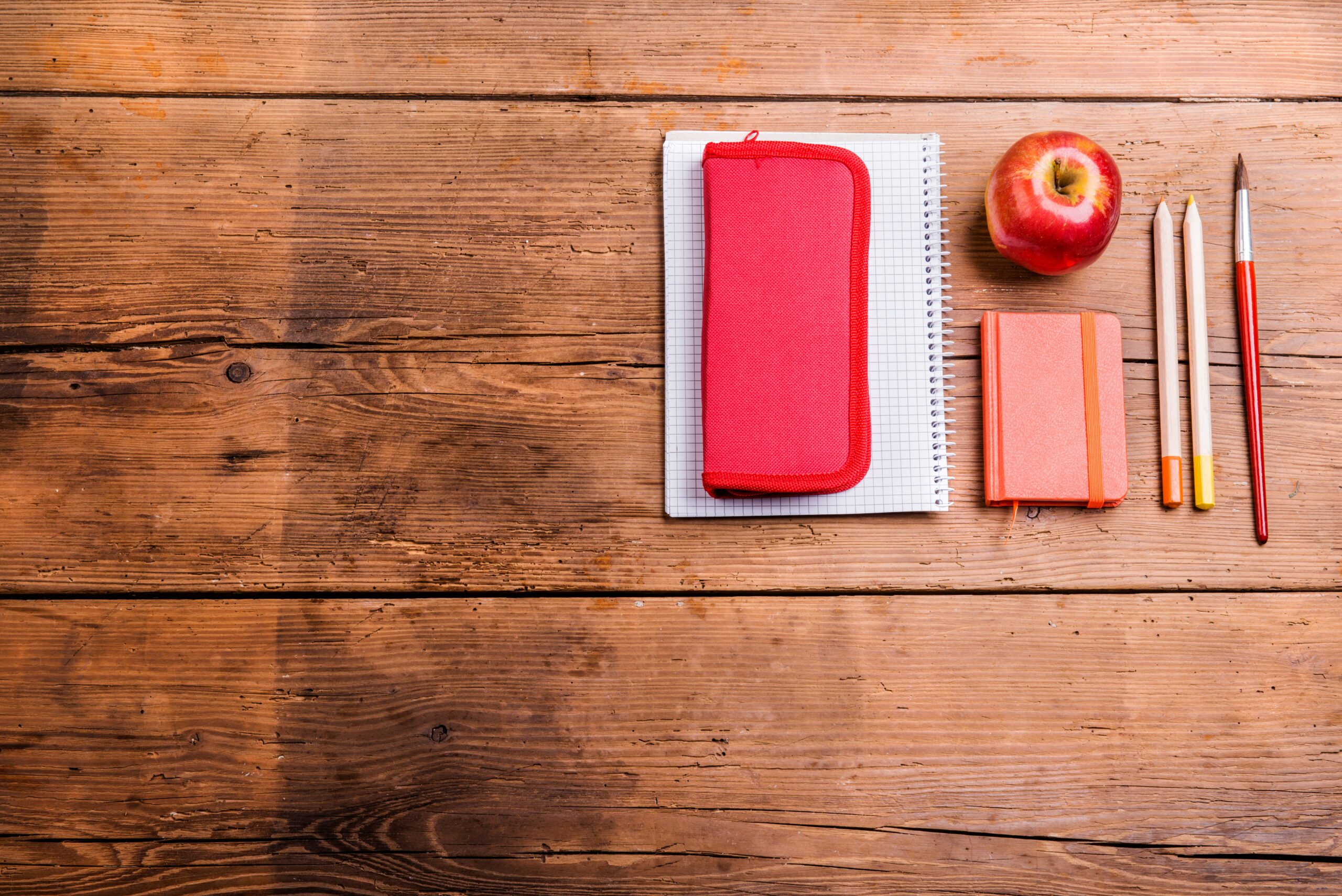 A wooden desk with school supplies and a red apple. 