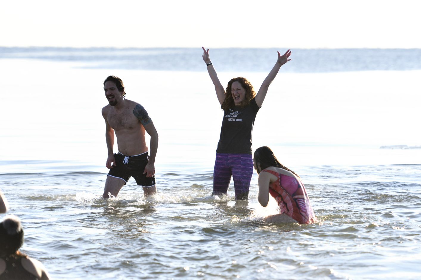 Landscape photo of three students standing in Long Island Sound. Woman in the center smiling with her hands in the air